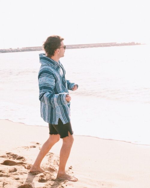 Buzo Cape color celeste como el cielo y el mar. Foto de modelo hombre caminando en la playa. Usando el buzo de manera práctica y cómoda