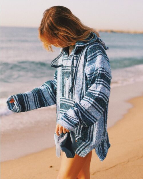 Buzo Cape color celeste como el cielo y el mar. Foto de modelo mujer caminando en la playa. Usando el buzo de manera práctica y cómoda